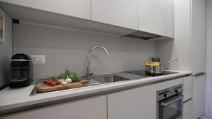 Uma cozinha moderna com uma pia de aço inoxidável, uma cafeteira e um tacho de espaguete na bancada.