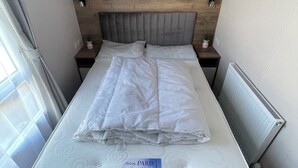 A neatly made bed with a mattress labeled 'Malvern Paris' in a room with a wooden headboard, bedside tables with lamps, and a radiator. - Unity Beach (Burnham-on-Sea)