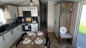 A modern kitchen with white cabinets, a dining table set for four, and a wooden bench. - Unity Beach (Burnham-on-Sea)