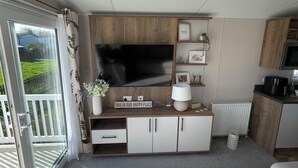 A modern kitchenette with a flat-screen TV, wooden cabinets, and a small dining area. - Unity Beach (Burnham-on-Sea)