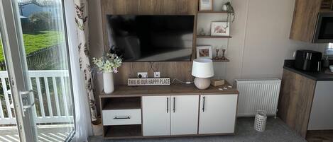 A modern kitchenette with a flat-screen TV, wooden cabinets, and a small dining area.