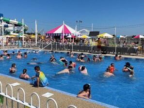 A swimming pool with people in the water, a fenced area, and a tent in the background.