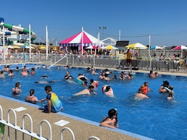 Una piscina con gente en el agua, un área cercada y una tienda de campaña al fondo.