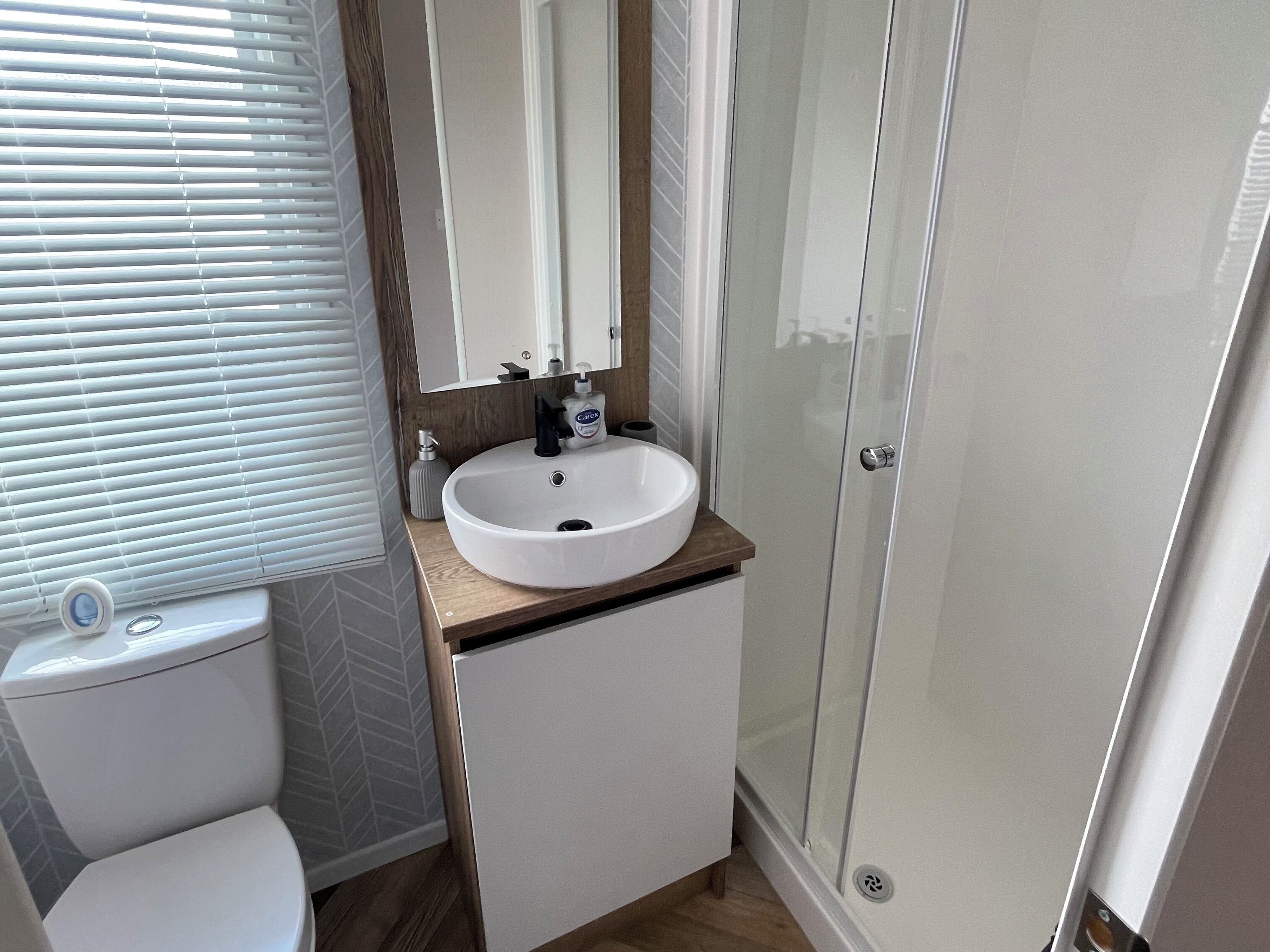 Un baño con lavamanos blanco, inodoro, espejo y cabina de ducha.