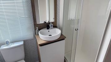 Un baño con lavamanos blanco, inodoro, espejo y cabina de ducha.
