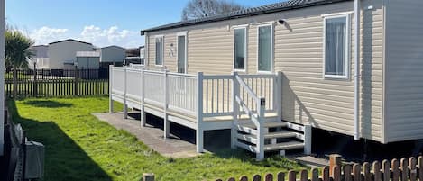 A mobile home with a porch and steps, surrounded by a wooden fence and a grassy yard.