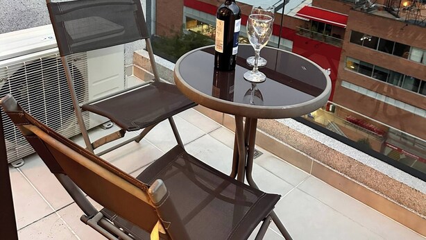 A balcony with a table, chairs, a bottle of wine, and a glass. - Premium Loft With AC Panoramic View in Laureles (Medellín)