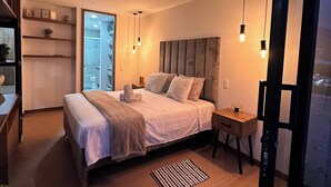 A modern bedroom with a bed, bedside tables, and a view of a cityscape through a large window. - Premium Loft With AC Panoramic View in Laureles (Medellín)