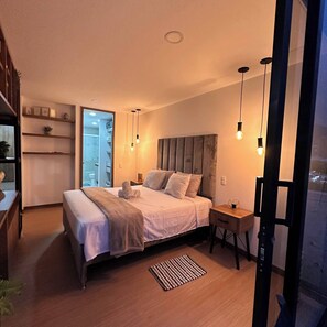 Ein modernes Schlafzimmer mit Bett, Nachttischen und Blick auf eine Stadtlandschaft durch ein großes Fenster.