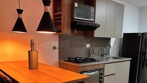 A modern kitchen with a wooden table, black pendant lights, a microwave, a stove, and a refrigerator. - Premium Loft With AC Panoramic View in Laureles (Medellín)