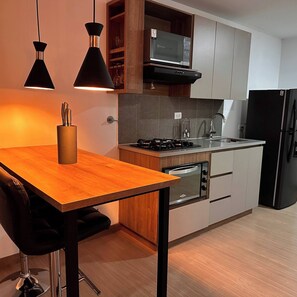 Eine moderne Küche mit einem Holztisch, schwarzen Pendelleuchten, einer Mikrowelle, einem Herd und einem Kühlschrank.