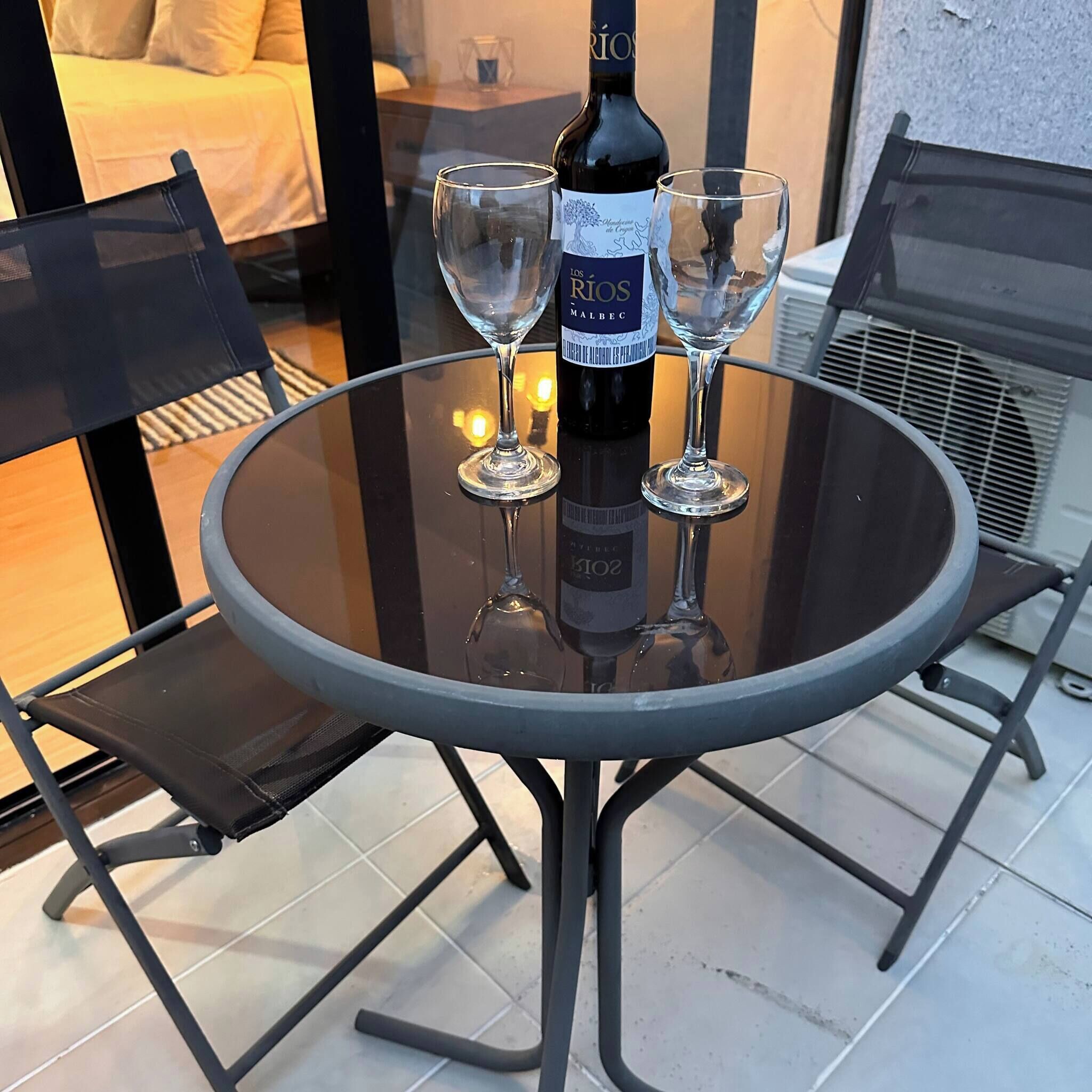 A round glass table with a wine bottle and two wine glasses on it.