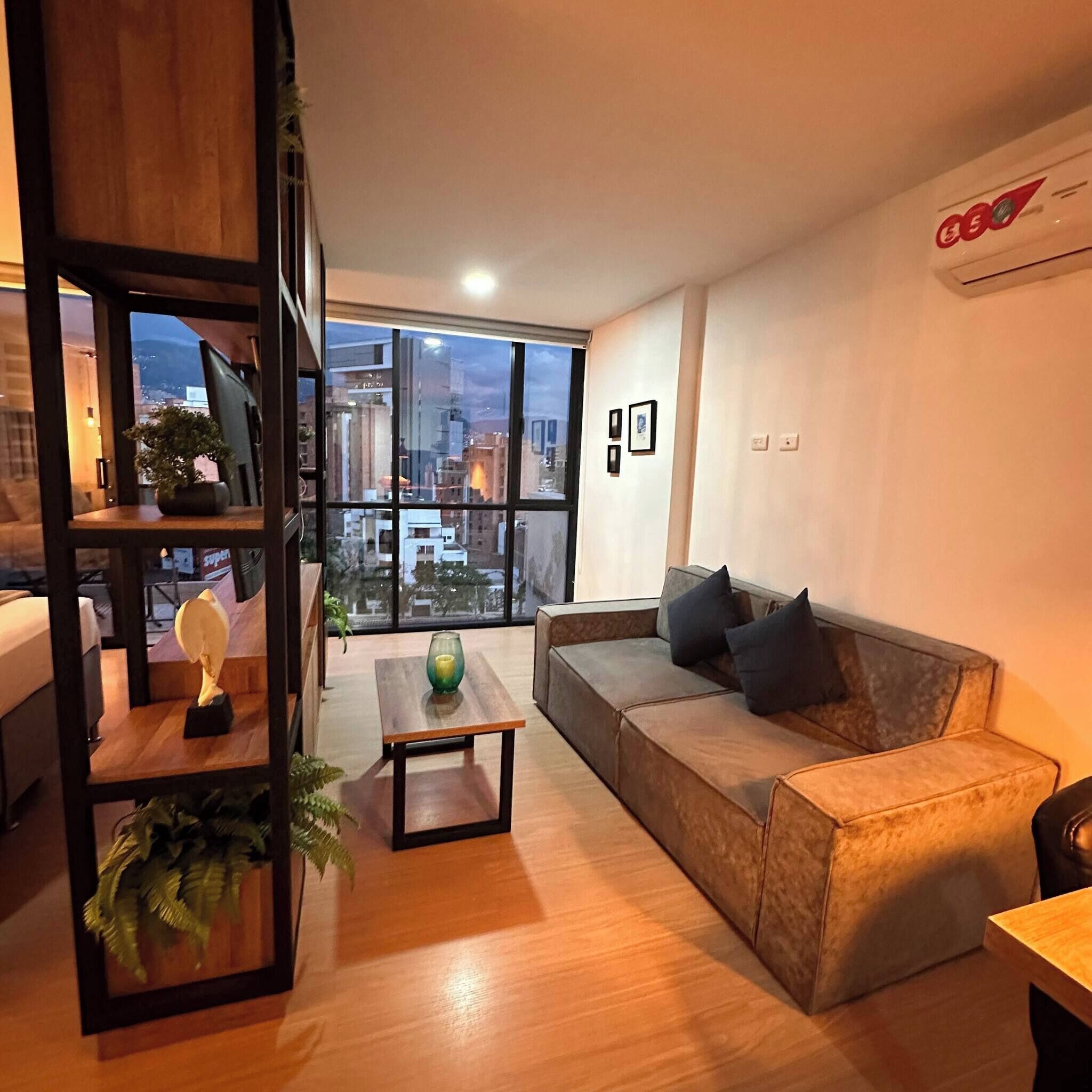 A modern living room with a large window, a sofa, a coffee table, and a bookshelf.