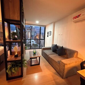 A modern living room with a large window, a sofa, a coffee table, and a bookshelf. - Premium Loft With AC Panoramic View in Laureles (Medellín)