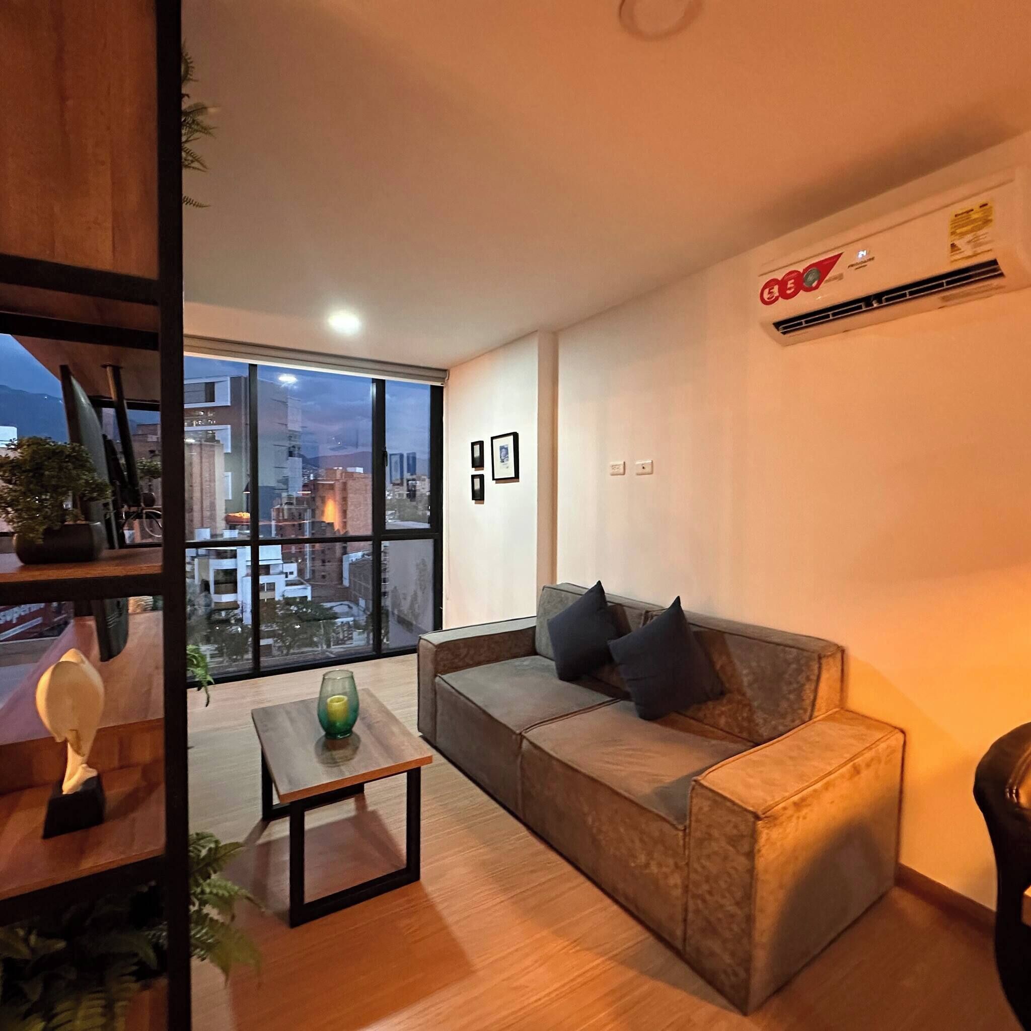 Ein modernes Wohnzimmer mit großem Fenster, einer Couch, einem kleinen Tisch und einer Klimaanlage.
