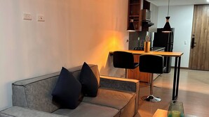 A modern living room with a grey sofa, two black chairs, a wooden table, and a kitchen in the background. - Premium Loft With AC Panoramic View in Laureles (Medellín)