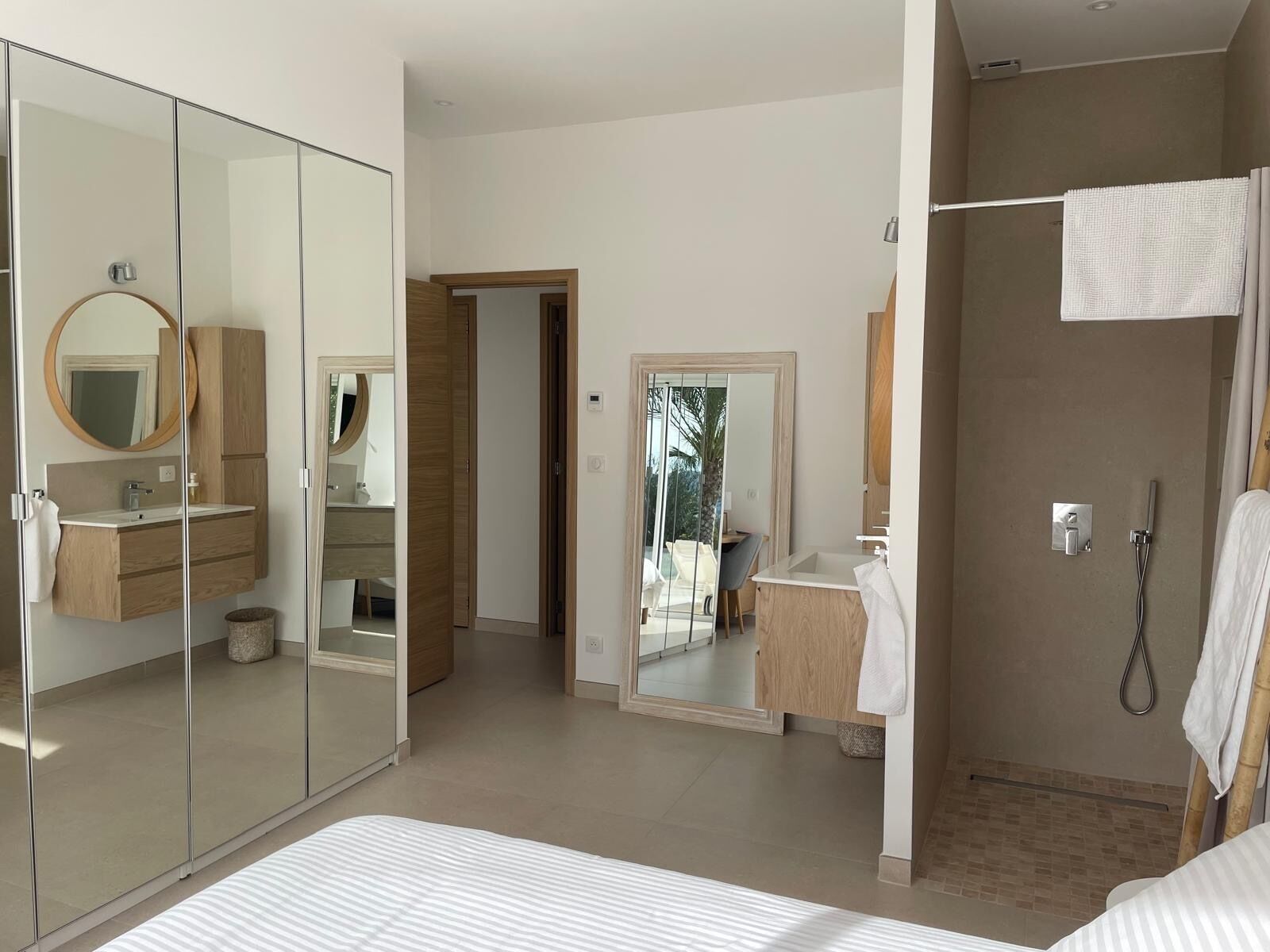 A modern bedroom with a large bed, a walk-in closet, a bathroom with a shower, and a mirror.