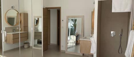 A modern bedroom with a large bed, a walk-in closet, a bathroom with a shower, and a mirror.