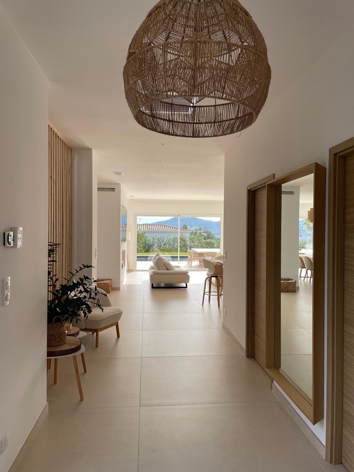 Un intérieur moderne agrémenté d’un grand luminaire suspendu en fibres tressées, d’un canapé et d’un coin repas baigné de lumière naturelle.
