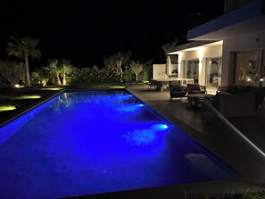 A swimming pool with a blue light, surrounded by outdoor furniture and a modern house. - Exceptional new contemporary villa with air conditioning, ocean views, a private pool, and a hot tub (Saint-Cyr-sur-Mer)