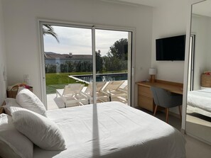 A bedroom with a bed, a desk, a chair, and a TV. There is a sliding glass door leading to a pool area. - Exceptional new contemporary villa with air conditioning, ocean views, a private pool, and a hot tub (Saint-Cyr-sur-Mer)