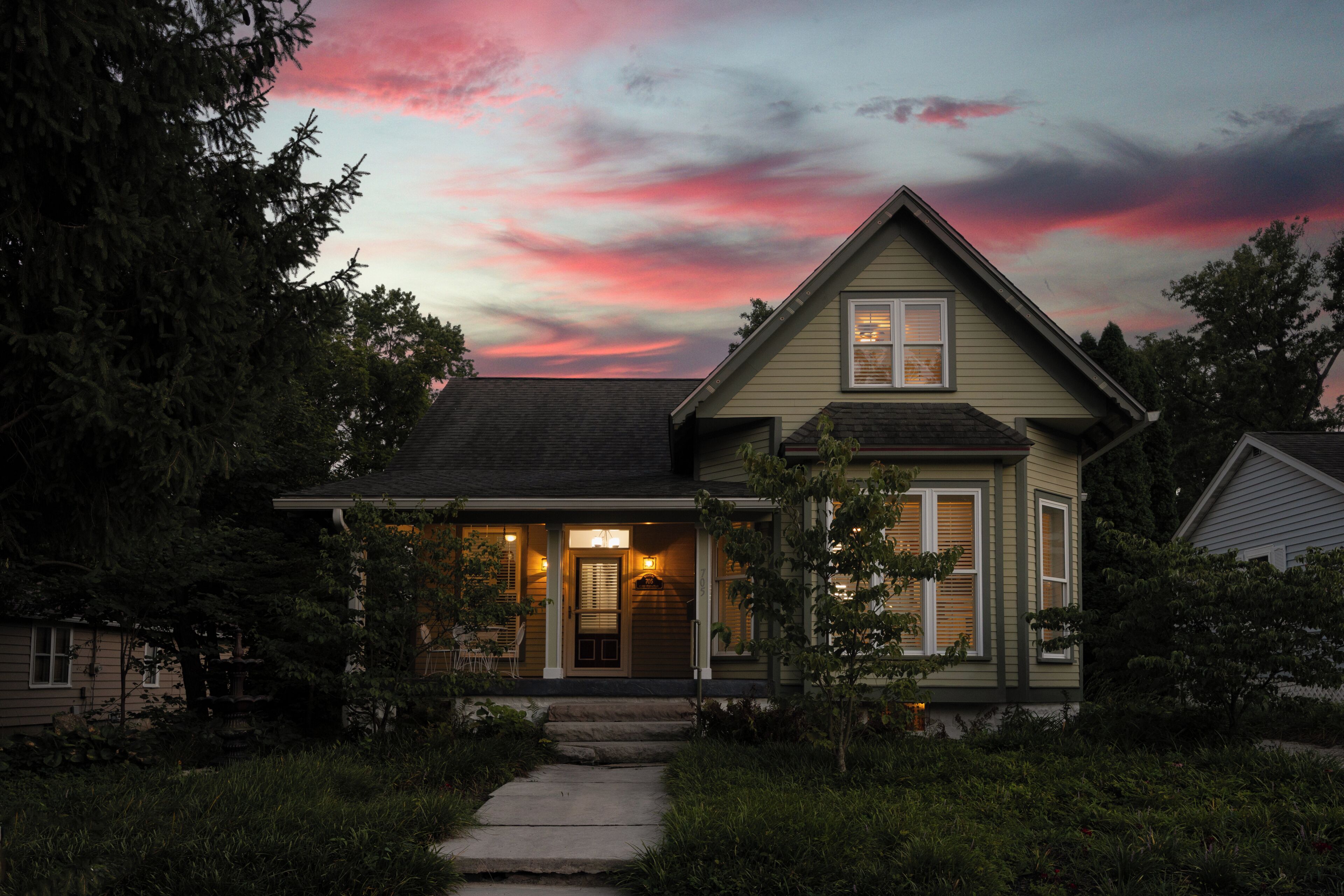 Ein zweistöckiges Haus mit Veranda, Hausnummer 705 an der Tür und einem klaren Himmel mit rosa und violetten Farbtönen im Hintergrund.
