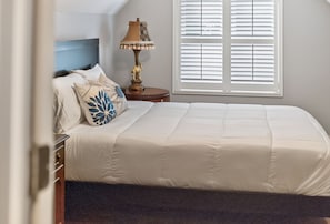 A neatly made bed with a white comforter, a decorative pillow, and a bedside lamp. - 4 Blocks to IU! 3BR Stay w/ Parking, Gym & FirePit (Bloomington)