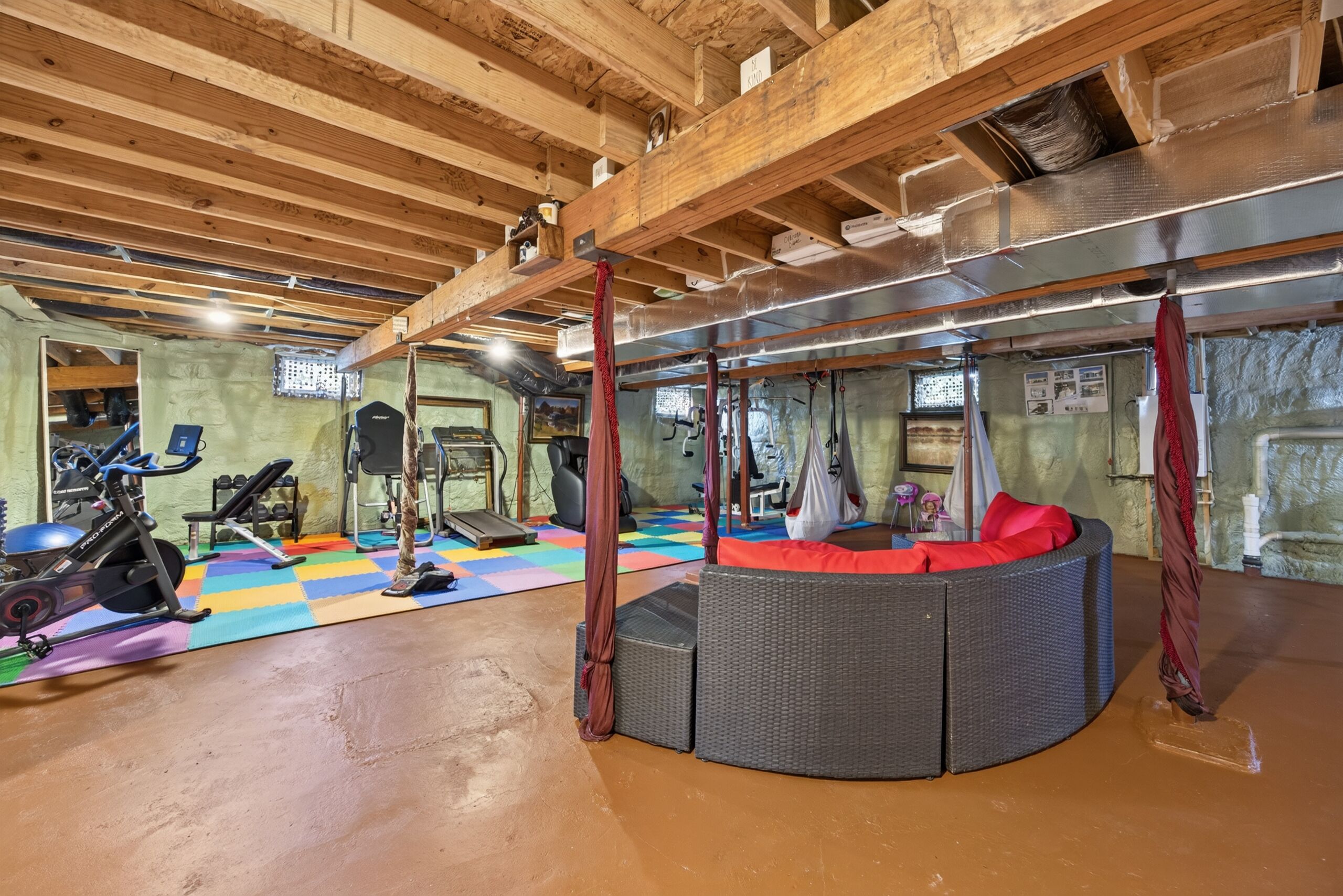 A gym with exercise equipment, a colorful floor mat, and a wicker sofa.