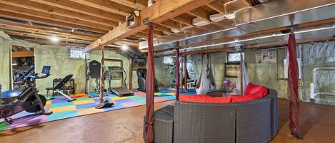 A gym with exercise equipment, a colorful floor mat, and a wicker sofa.