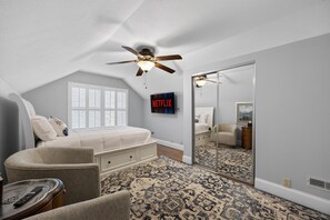 A bedroom with a sloped ceiling, a ceiling fan, a bed, a chair, a TV, and a large mirror. - 4 Blocks to IU! 3BR Stay w/ Parking, Gym & FirePit (Bloomington)