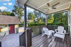A covered porch with a ceiling fan, white Adirondack chairs, and a red door. - 4 Blocks to IU! 3BR Stay w/ Parking, Gym & FirePit (Bloomington)