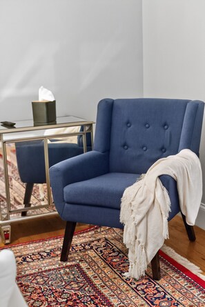 A blue armchair with a white throw blanket, a glass side table with a tissue box, and a patterned rug. - Black Walnut - 4 Blocks to Kirkwood / Downtown w/ at home Gym (Bloomington)