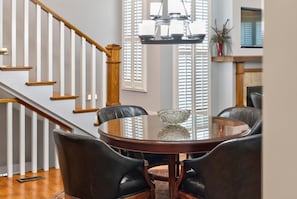 A dining area with a round table, four chairs, a chandelier, and a staircase with wooden railings. - 4 Blocks to IU! 3BR Stay w/ Parking, Gym & FirePit (Bloomington)