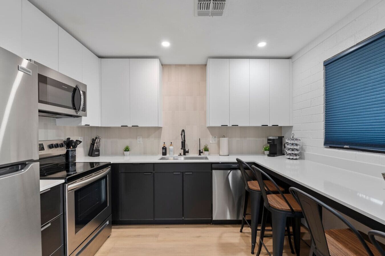 A modern kitchen with white cabinets, a black countertop, stainless steel appliances, and a bar area with stools.