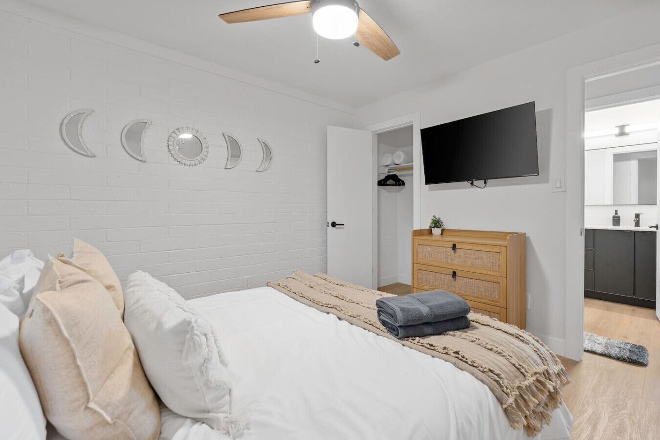 Une chambre à coucher comprenant un lit, un téléviseur, une commode en bois et un mur décoré de motifs représentant les phases de la lune.