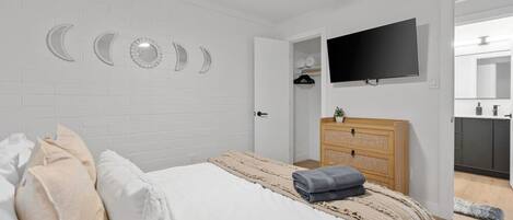 Un dormitorio con cama, televisor, cómoda de madera y pared decorada con fases lunares.