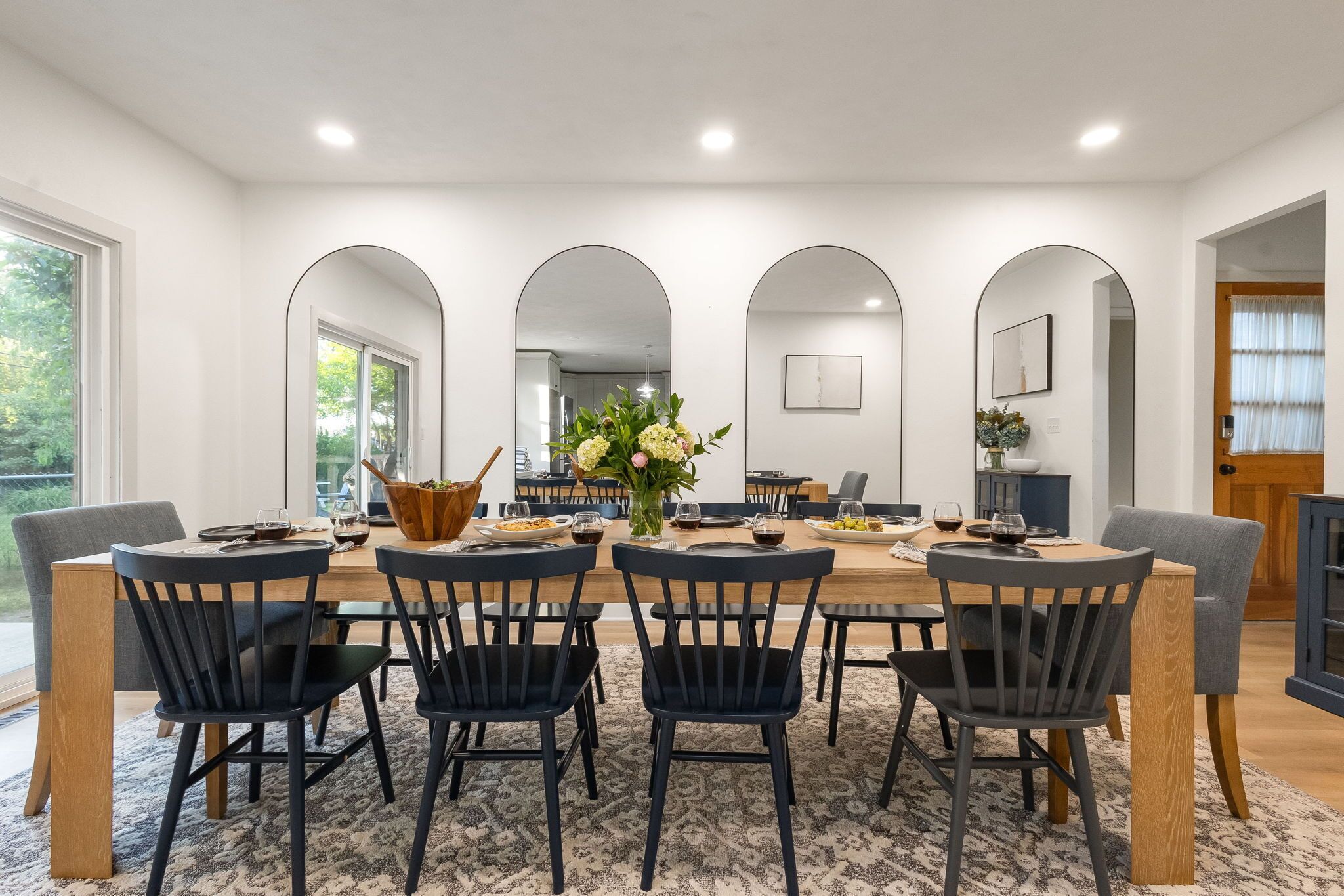 A dining area with a long table, black chairs, and a central vase with flowers.