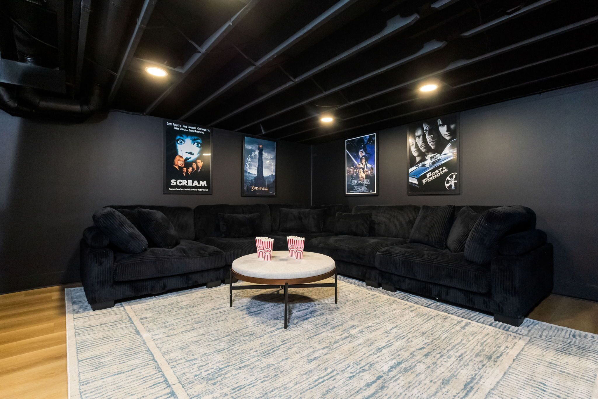 A dark-themed room with a sectional sofa, a coffee table, and movie posters on the wall.