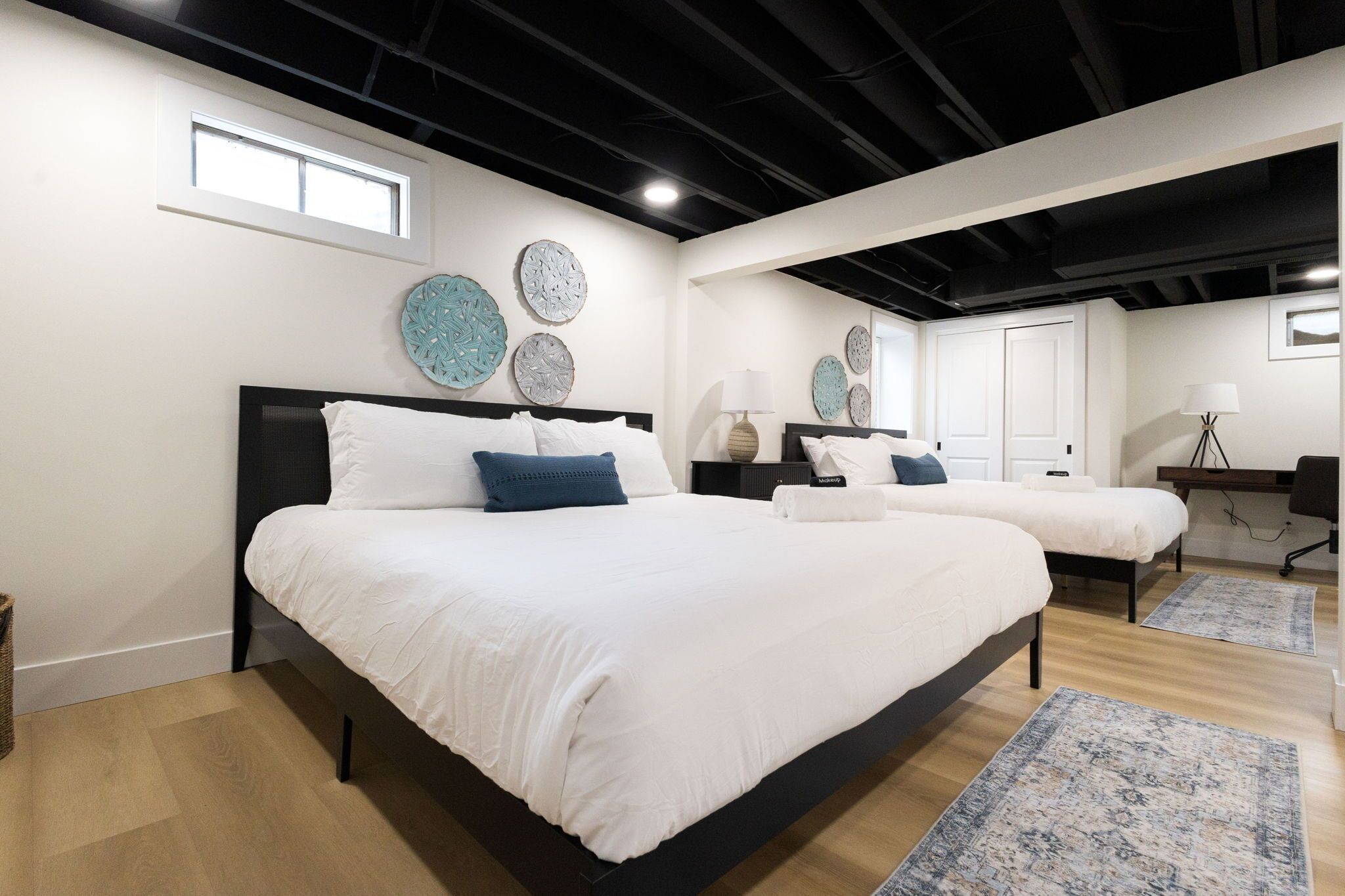 Une chambre moderne avec un grand lit, un plus petit lit, un bureau et une chaise. On y trouve également des éléments décoratifs sur les murs et une fenêtre.