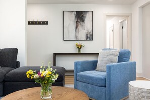 A modern living room with a blue armchair, a dark sofa, and a round wooden coffee table with a vase of flowers. - Theater · HotTub · PoolTable · Walk ND · Sleeps 12 (South Bend)