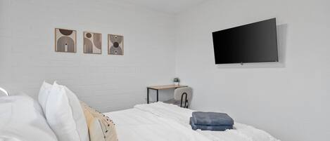 Un dormitorio con una cama, un escritorio y un televisor montado en la pared.