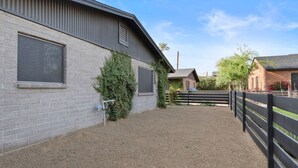 A stable with a gravel driveway, a black fence, and a brick building in the background. - Biltmore 2BR Bungalow - Desk, Parking, Patio (Phoenix)