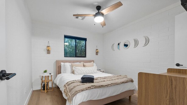 A bedroom with a bed, a ceiling fan, a window, and a wall with decorative mirrors. - Biltmore 2BR Bungalow - Desk, Parking, Patio (Phoenix)