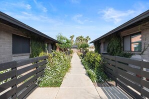 A pathway flanked by two buildings with brick walls and wooden fences, leading to a clear sky. - Biltmore 2BR Bungalow - Desk, Parking, Patio (Phoenix)