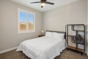 A bedroom with a bed, a nightstand, a lamp, a ceiling fan, a window with blinds, and a shelf with a statue. - Bright & Modern Home w/ Open Living, Great Area, & Perfect for Families! (Sun City West)