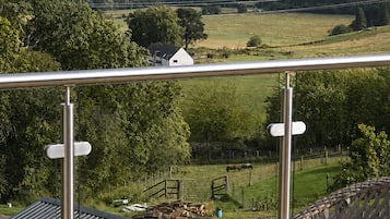 A balcony with a view of a rural landscape, including fields and hills.