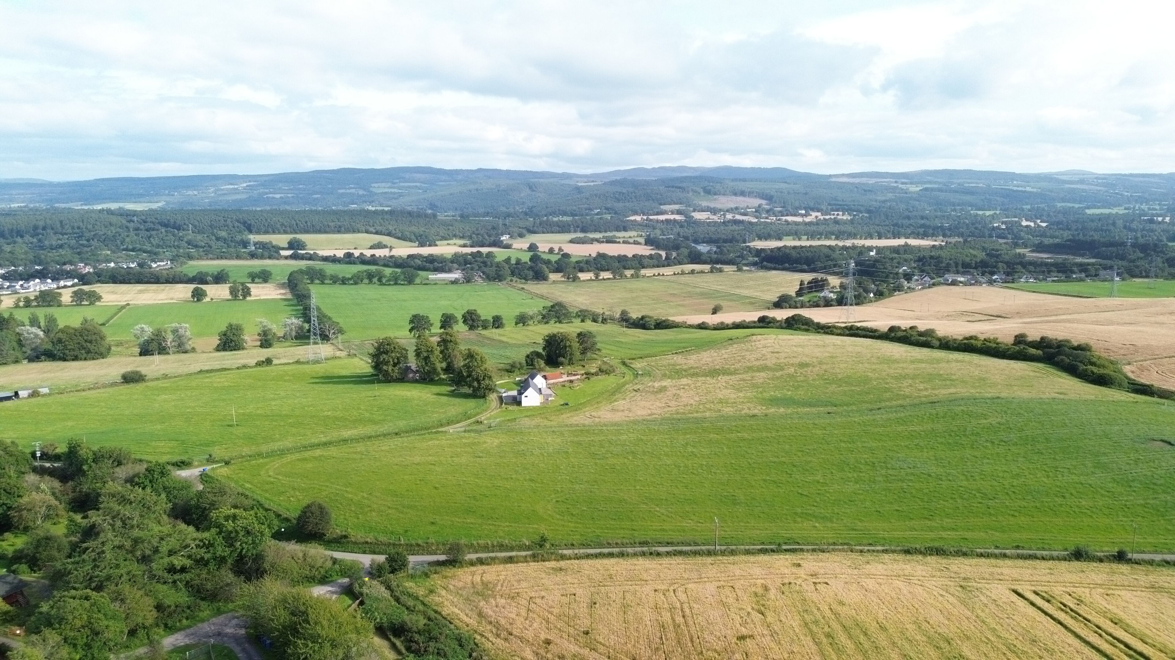 A rural landscape with fields, a small white building, and distant hills.