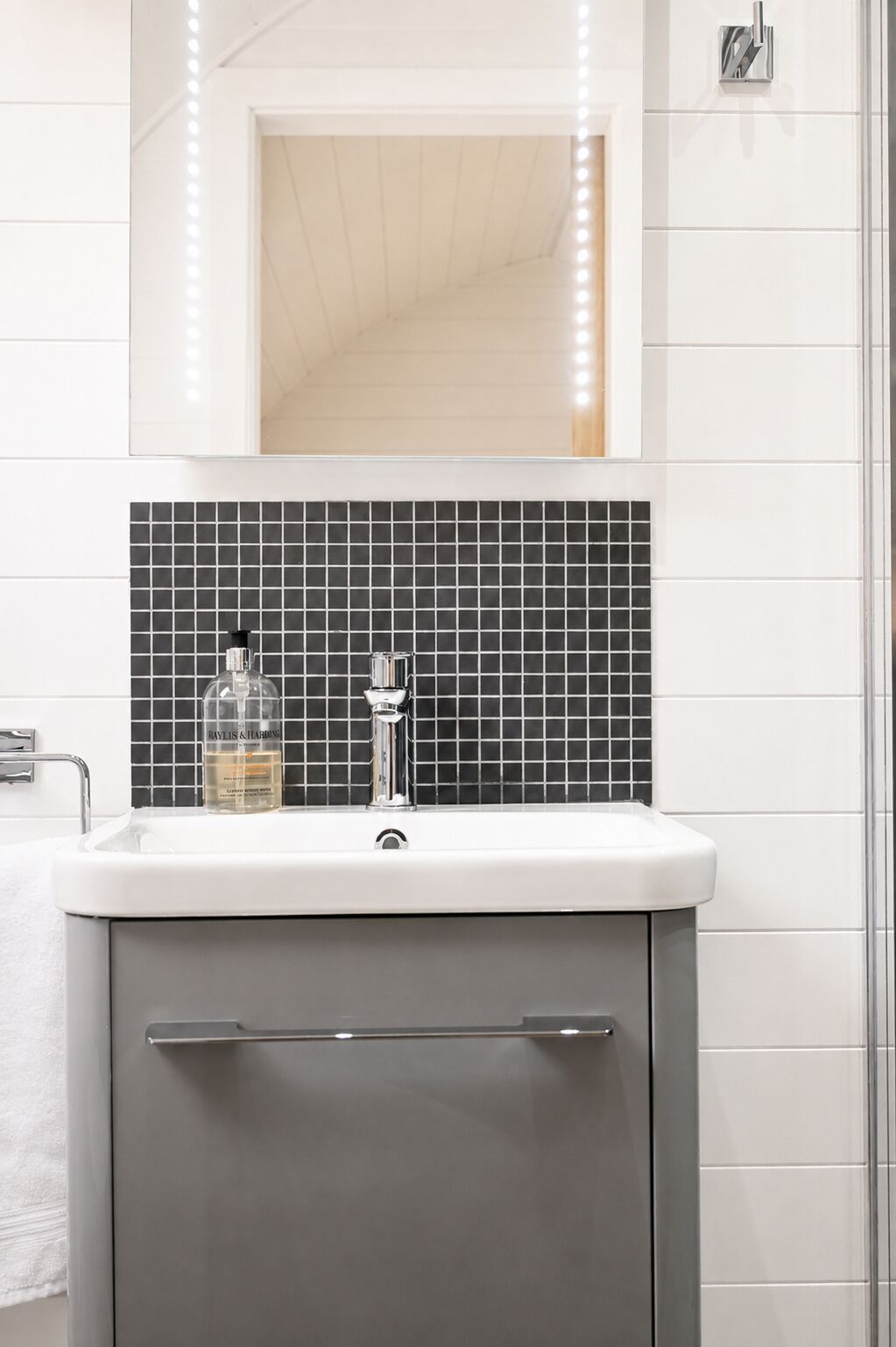 A bathroom with a white sink, a mirror above it, and a black tiled backsplash.