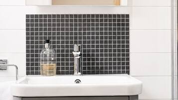 A bathroom with a white sink, a mirror above it, and a black tiled backsplash.