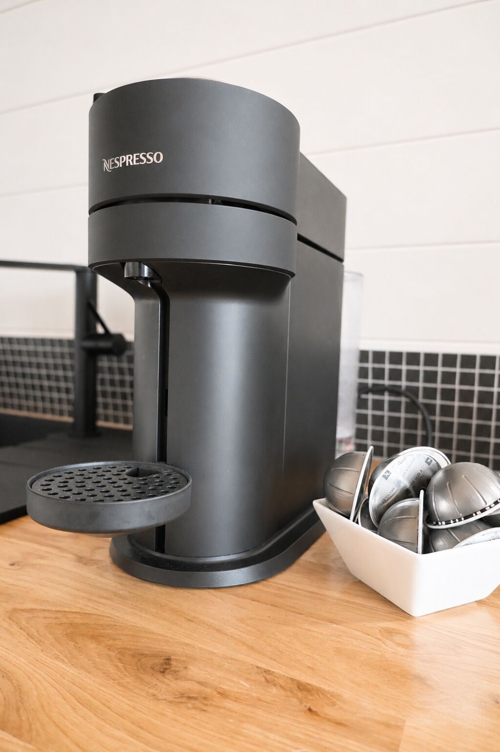 Una máquina de café Nespresso negra con un recipiente para goteo y un escurreplatos con utensilios.